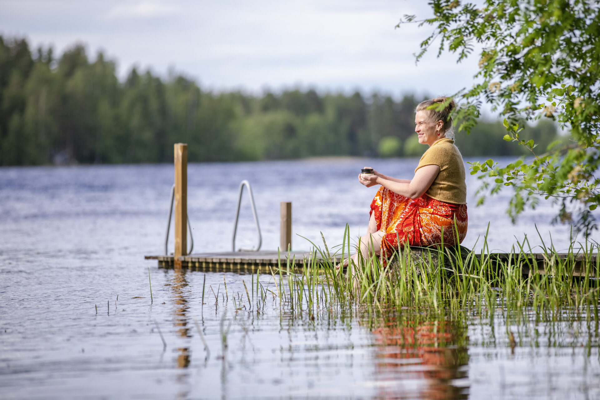 Nainen juo kahvia laiturilla järven rannassa