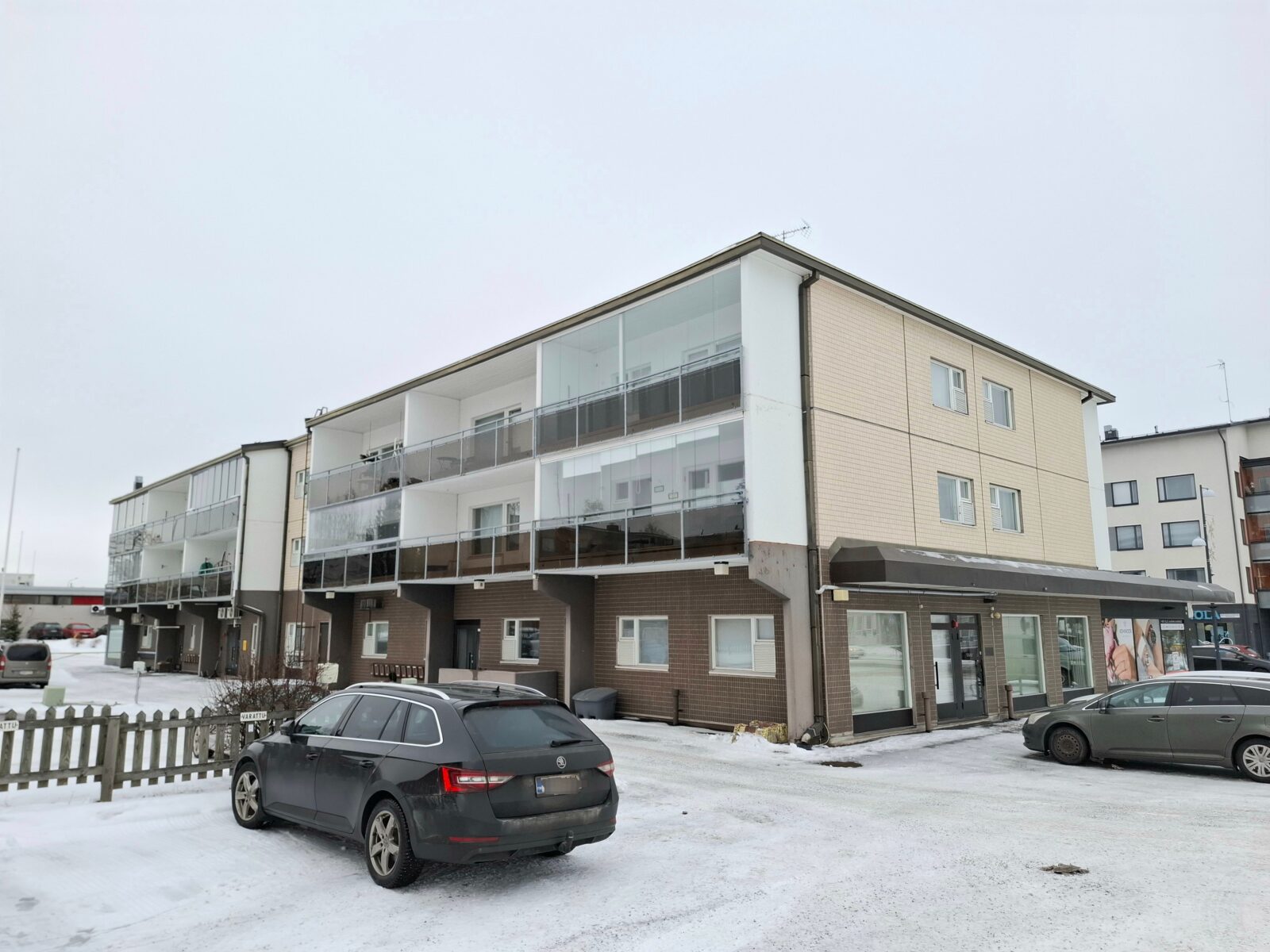 Rakennus talvella ulkoapäin, matala kerrostalo, edessä auto.