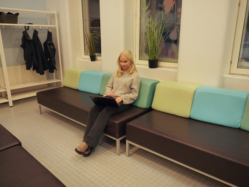 Nuori nainen istuu sohvalla kannettava tietokone sylissään.