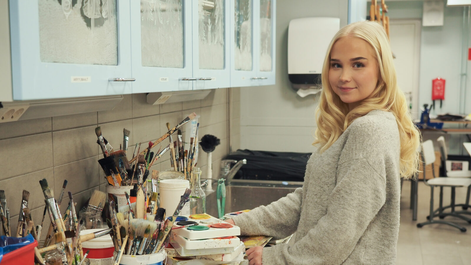 Nuori henkilö Jämsän lukion kuvataideluokassa, pöydän äärellä valitsemassa sivellintä.