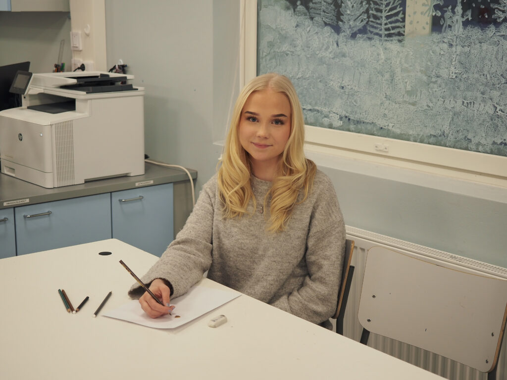 Nuori nainen istuu piirtämässä pöydän ääressä Jämsän lukiolla.