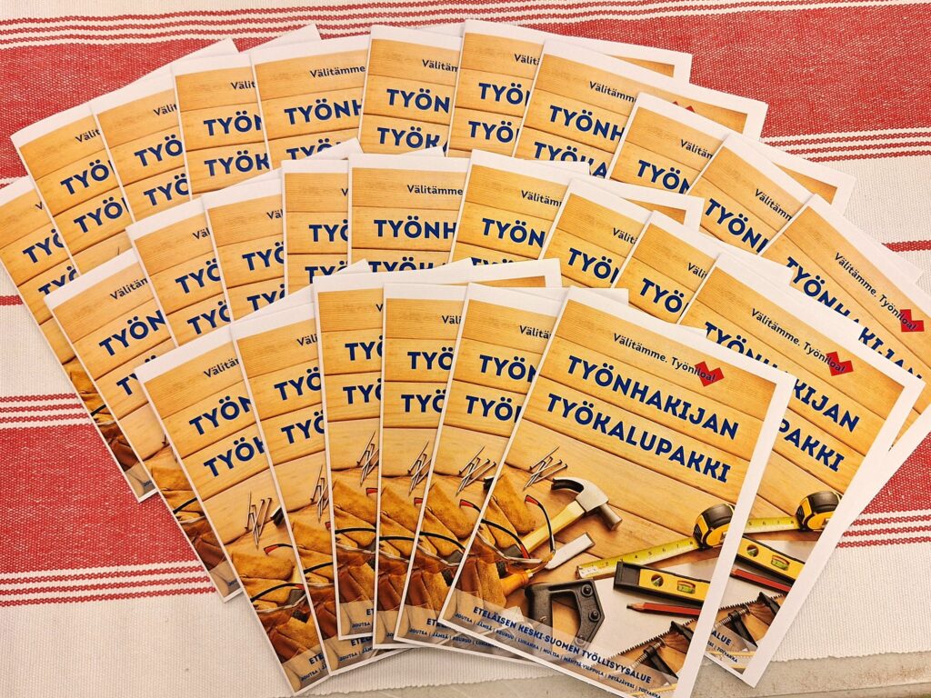 Esitteitä levitettynä pöydälle. Esitteen kannessa kuvia työkaluista ja teksti Työnhakijan työkalupakki.