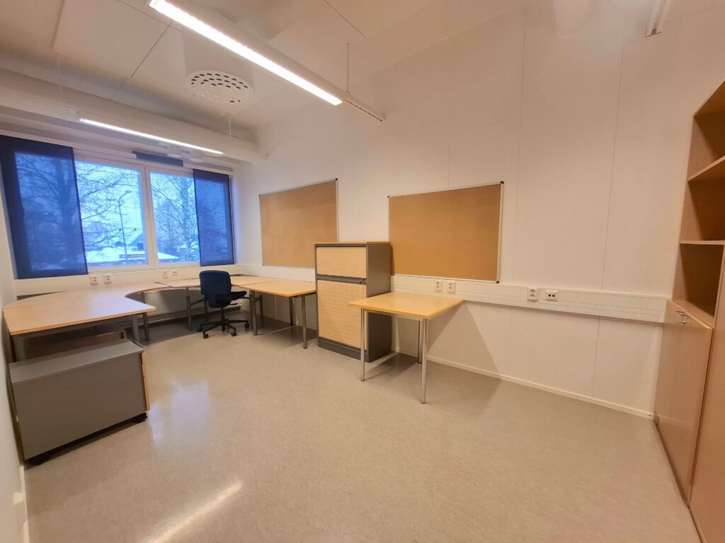 Huoneessa pöytiä, ikkuna ja tuoli, toimistotila.