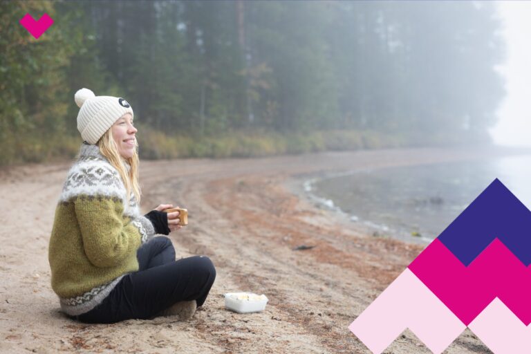 Henkilö istuu rannalla kuksa kädessään.