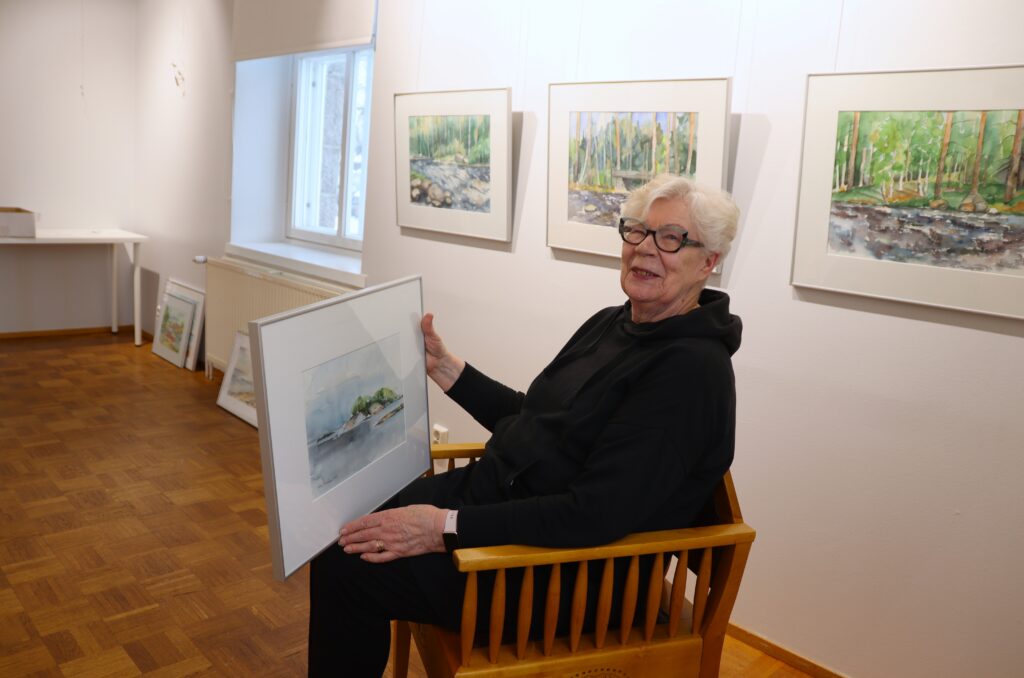 Taiteilija istuu taulu sylissään Galleria Kivipankissa.