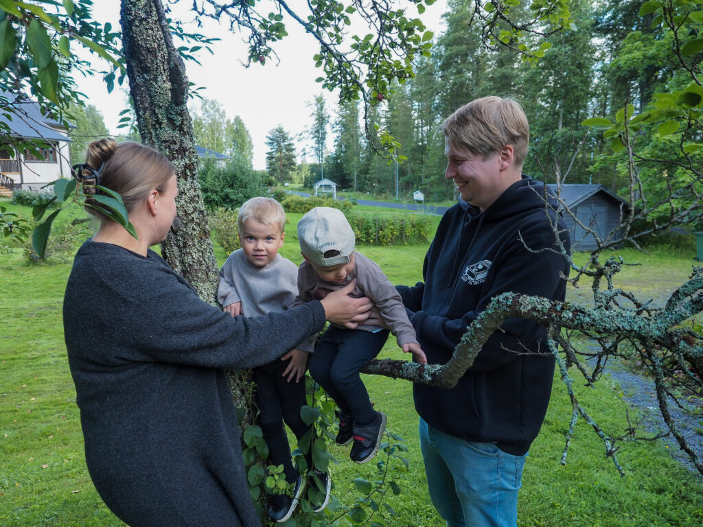 Kaksi aikuista ja kaksi lasta, lapset istuvan puun oksalla.