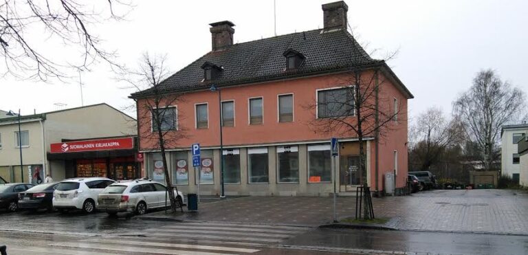 Rakennus ulkoapäin, katua, autoja ja punertava rakennus.