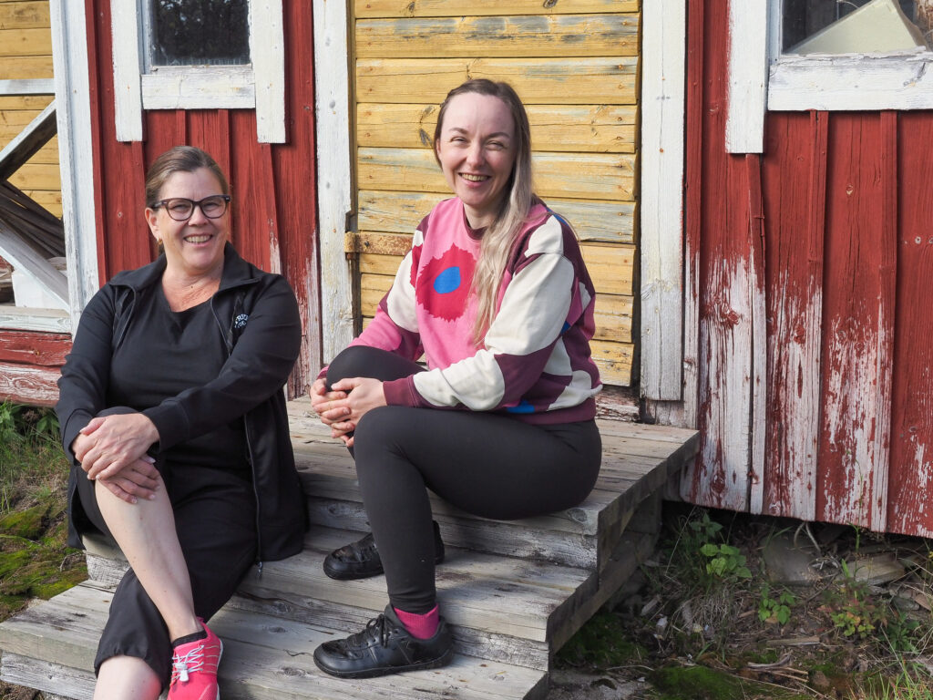 Kaksi ihmistä istuu rappusilla ulkona, aurinkoinen keli.